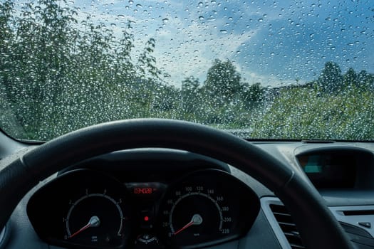 Raindrops on windshield with steering wheel in the car and sky