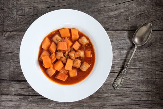 Pumpkin and bratwurst as goulash with spoon in silver on rustic table