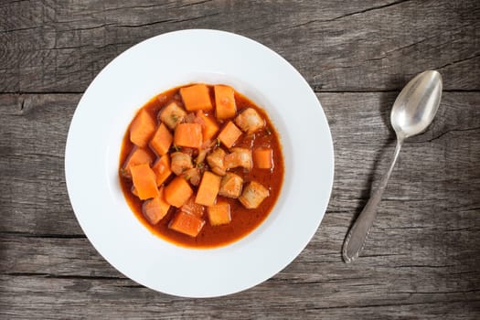 Goulash with pumpkin and bratwurst in plate with spoon