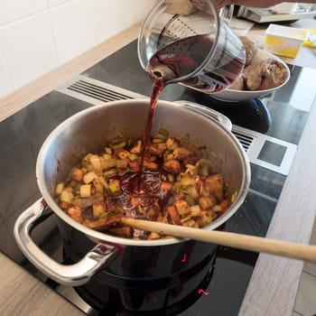 Female hand deglazes vegetables in the pot when frying with red wine