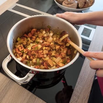 Hand does stew vegetables with a wooden spoon in a saucepan