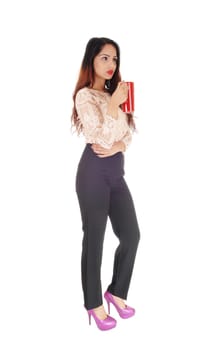 A gorgeous young business woman in a beige blouse and black trousers.holding a red big coffee mug, looking serious, over white background.