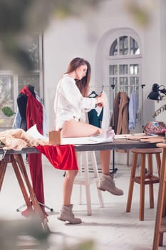 The female fashion designer working in studio sitting on the desk