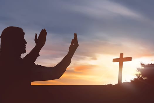 Silhouette man raising hand while praying to jesus on sunset background