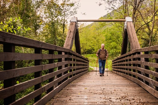 Mature man are hiking in the mountains, walking on a wooden bridge