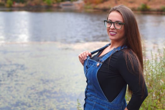young woman wearing jeans in a park water lake glasses brown hairs portrait outdoor
