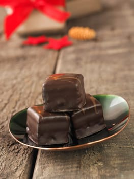 Tasty sweet chocolate dices on a green plate, Christmas bakery or pastry concept, Gift boxes and Christmas decoration in the background