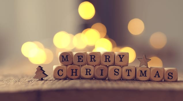 Christmas card with the words Merry Christmas on a wooden table, blurred Christmas lights in the background