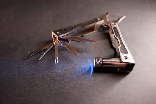 Combined pliers, multifunctional, with flashlight. Against the background of a gray texture.