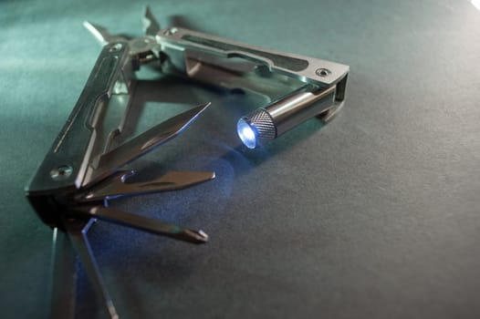 Combined pliers, multifunctional, with flashlight. Against the background of a gray texture.