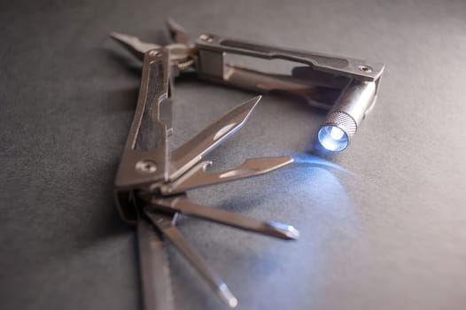 Combined pliers, multifunctional, with flashlight. Against the background of a gray texture.