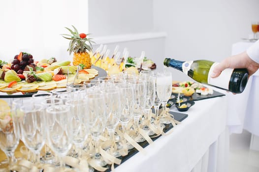 A beautiful fruit bar serving a festive table. The waiter pours champagne in wine glasses.
