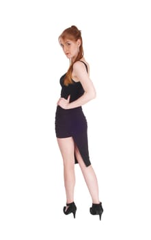 A beautiful slim woman in a black dress and long brunette hair standing.from the back, looking over her shoulder, isolated for white background.