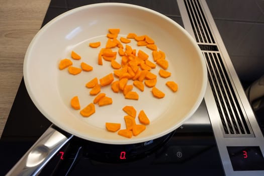 Carrots in frying pan on induction cooker with cooktop extractor in the middle