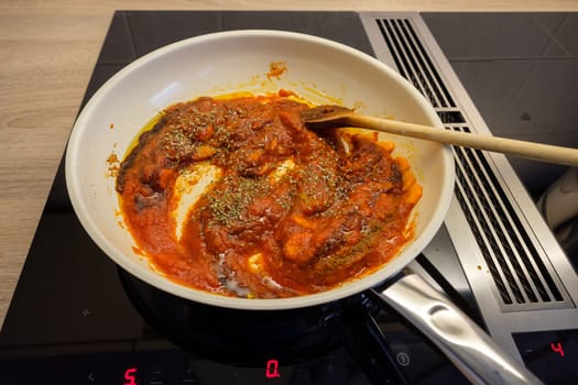 Frying pan on stove with cooking spoon and tomato sauce with oregano