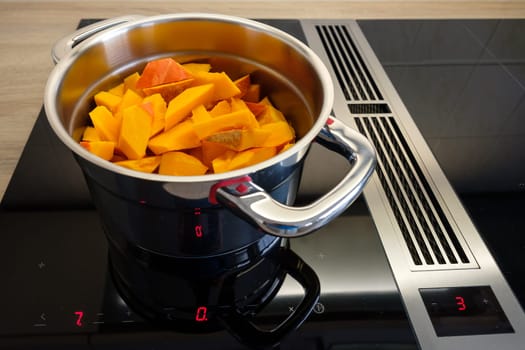 Pot with orange pieces of pumpkin on hob with induction