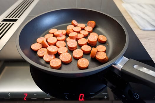 Coated frying pan with sausage on the stove for induction