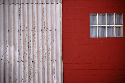 The close-up of a window made of glass tiles on a red painted wall with adjacent corrugated iron.