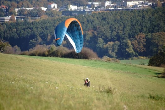 A paraglider stands on a hill and directs his paraglider.