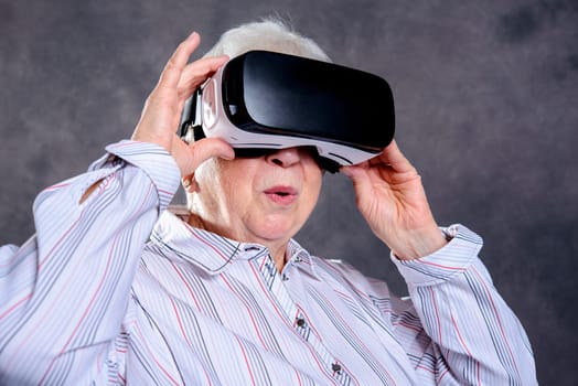 gray hairy elderly woman using virtual reality glasses and looking surprised