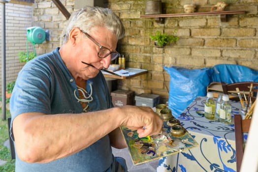 Senior Man squeezing oil color on a wood palette