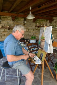 Senior Man painting a picture with oil colors, cleaning the brush