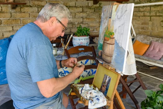Senior Man painting a picture with oil colors, cleaning the brush