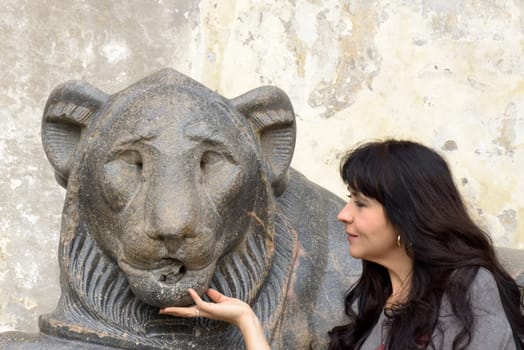 A beautifl girl posing near a lion sculpture in a public square in Rome. She is touching the chin of the Lion
