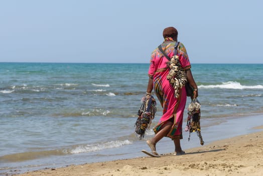 Rome, Italy - August 13, 2015: a black woman walking and selling necklaces and bracelets on the beach