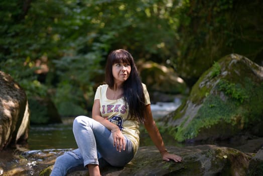 Nice girl posing on a rock in the middle of a little river