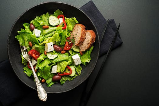 Green salad with cheese and fresh vegetables on a black background. Greek salad.