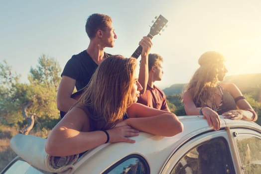 Group of happy people in a car at sunset in summer.