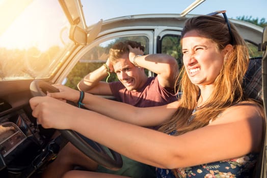 Couple in a car at sunset, with happy girl driving fast and boy scared, screaming and praying.