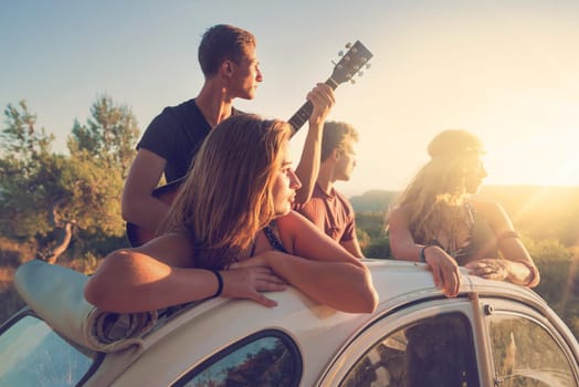 Group of happy people in a car at sunset in summer.