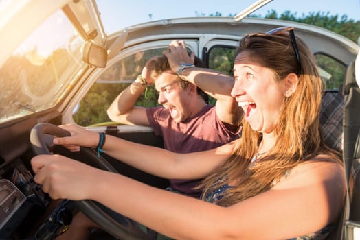 Couple in a car at sunset, with happy girl driving fast and boy scared, screaming and praying.