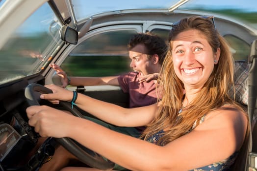 Couple in a car at sunset, with happy girl driving fast and boy scared, screaming and praying.