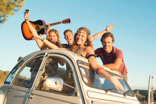 Group of happy people in a car at sunset in summer.