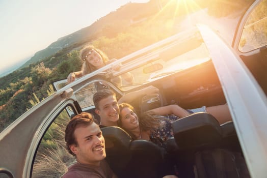 Group of happy people in a car at sunset in summer.