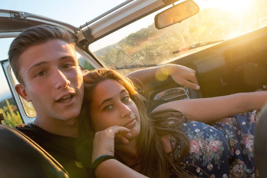 Happy young couple in a car enjoying the beautiful sunset in countryside.