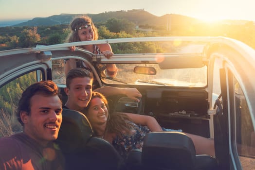 Group of happy people in a car at sunset in summer.