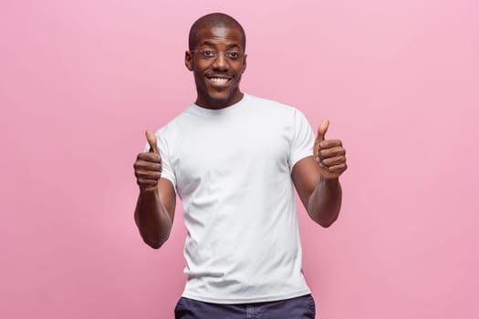 Portrait of a very happy afro american man showing thumbs up in studio on pink background