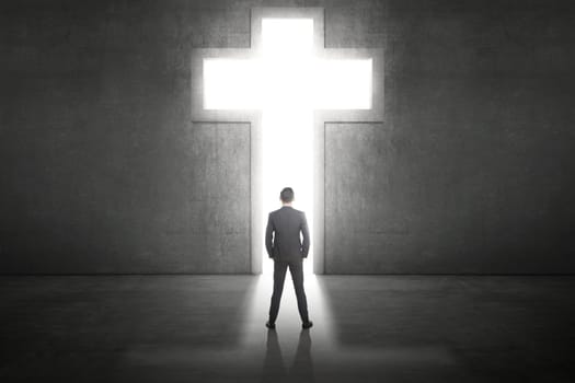 Business man standing in front of the shining cross on the wall