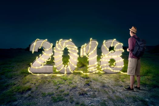 Traveling man looking 2018 number with christmas light decoration on the field. Happy New Year 2018