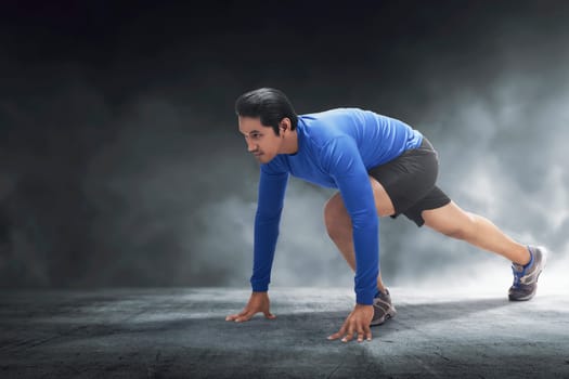 Muscular asian man ready for run with concrete floor background