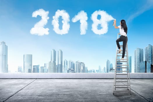 Business woman using stair spraying white cloud with 2018 shape on the building rooftop