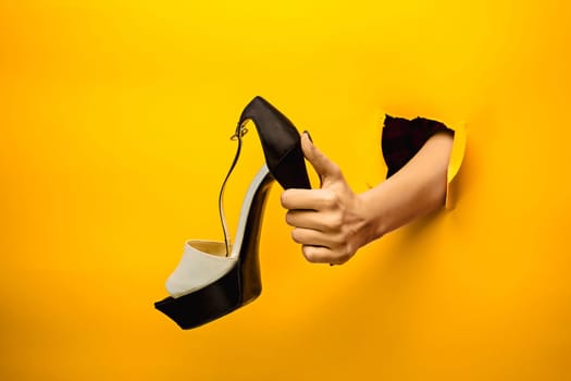 The female shoe on hand through a torn yellow paper