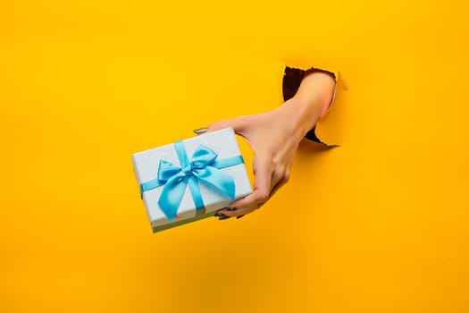 The close-up of female hand holding a present through a torn yellow paper, isolated