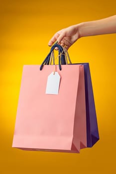 Female hand holding bright shopping bags on yellow