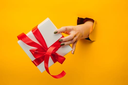 The close-up of female hand holding a present through a torn yellow paper, isolated