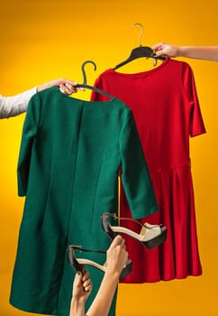 Textile, design, clothing, fashion concept. The female hands with dresses in her hands on yellow